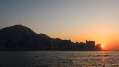 Batı Kowloon Rıhtım Alanı, Batı Kowloon Kültür Bölgesi, Hong Kong - 24 Aralık 2025: Victoria Limanı, Victoria Tepesi ve gökdelenleri gün batımında, güneş suyun üzerinde.