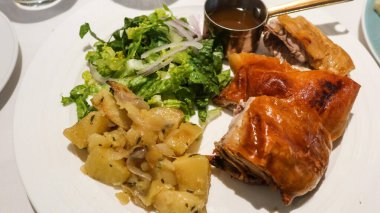 İspanyol usulü kavrulmuş, çıtır çıtır derili süt domuzu yanında otla baharatlı patates, taze yeşil salata ve fotokopi alanı olan beyaz bir tabakta zengin kahverengi sos.