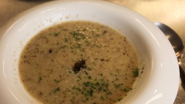 Beyaz kase kremalı mantar çorbasına yakın doğranmış otlarla süslenmiş, metalik bir yüzeyde fotokopi alanı ile servis edilmiş.