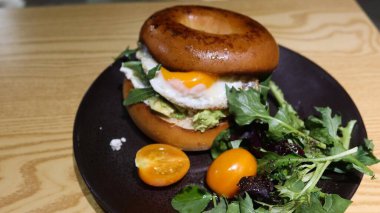 Yumurta, avokado ezmesi ve roket sebzesi, salata ve vişne domatesli simit dolu siyah tabakta fotokopi alanı ile birlikte.