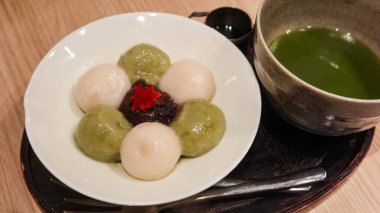 Japon kibrit mochi setine çeşitli renkli dango topları (beyaz ve yeşil çay), kırmızı fasulye macunu dolgusu, akçaağaç yaprağı garnitürü, köpüklü kibrit çayı ile sunulan laktar.