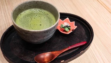 Geleneksel Japon kibrit çayını (yeşil çay) köpüklü yüzeyi olan kırsal seramik bir kasede akçaağaç yaprağı tepside ahşap bir kaşıkla renkli kaya benzeri çikolata ile servis edilir.