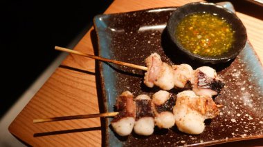 close up of two pieces of chargrilled Cuttlefish head skewer, the sweet and sour sauce on the side with copy space