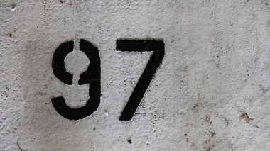 97 numara (doksan yedi) beyaz zeminde siyah ile boyanmış, kopyalanmış ve eskimiş görünüyor.