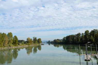 Fraser Nehri, Fort Langley, British Columbia, Kanada: Durgun nehir kenarı rıhtımı kano ve teknelerle dolu, yemyeşil ve sonbahar renkli ağaçlarla çevrili, gündüz vakti parçalı bulutlu bir gökyüzü altında