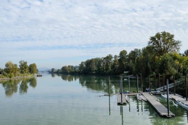 Fraser Nehri, Fort Langley, British Columbia, Kanada: Durgun nehir kenarı rıhtımı kano ve teknelerle dolu, yemyeşil ve sonbahar renkli ağaçlarla çevrili, gündüz vakti parçalı bulutlu bir gökyüzü altında