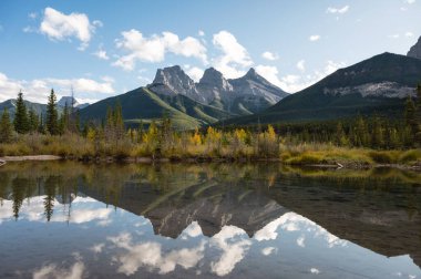 Üç Kız Kardeş Dağının Sahnesi Kanada 'nın Canmore kentindeki Bow River' da sonbahar ormanlarında yansıyor.