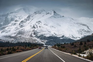 Otoyoldaki araba ve karlı dağ sırası Icefields Parkway, Kanada 'da kasvetli