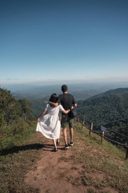 Genç Asyalı çift, tatilde tepenin üstünde sarılıp yürüyorlar.