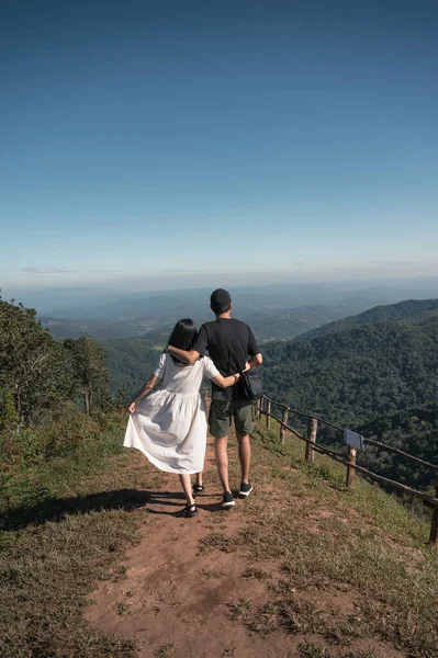 Genç Asyalı çift, tatilde tepenin üstünde sarılıp yürüyorlar.