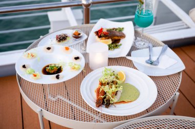 Beyaz tabakta çeşitli deniz ürünleri ve güvertedeki terasın verandasındaki mavi kokteyl.