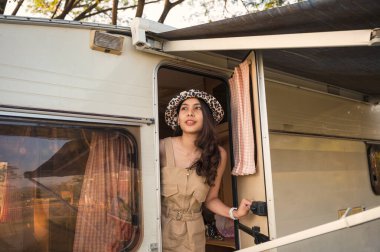 Güzel, Asyalı bir kadın, tatil için kamp alanındaki karavanda şapka takıyor.