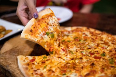 Kadın eli, dolmalık biberli, ahşap tepsiden bir dilim et pizzası, domates ve peynir alıyor.