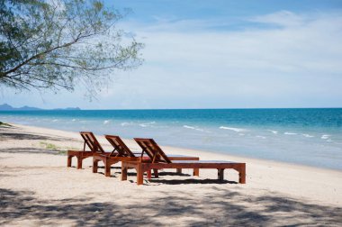 Yaz mevsiminde tropikal denizde plajda üç tahta güneş yatağı.