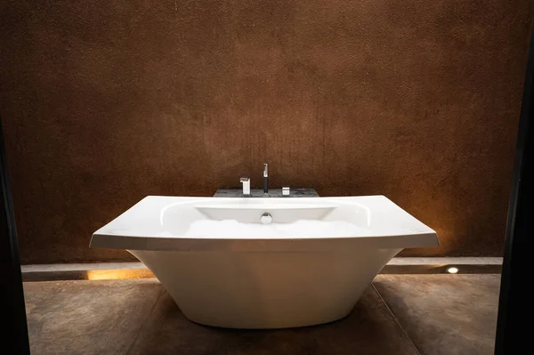 天然土色浴室中优雅的白色泡沫陶瓷浴缸 — 图库照片
