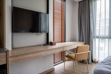 Yatak odasının içi rahat ahşap tarzıyla tasarlanmış. Ahşap masa ve perdede güneş ışığı olan sandalye.