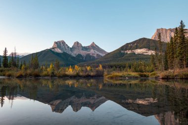 Kayalık dağlardan oluşan üç kız kardeş sabah Canmore, Banff Ulusal Parkı, Kanada 'daki yaylı nehirde yansıyor.