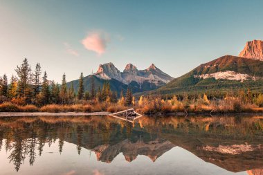 Kayalık dağlardan oluşan üç kız kardeş sabah Canmore, Banff Ulusal Parkı, Kanada 'daki yaylı nehirde yansıyor.