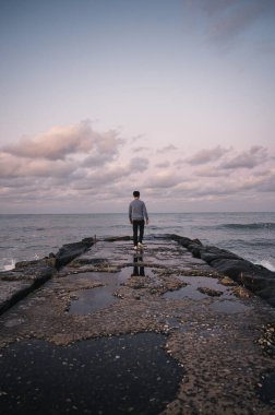 Jumunjin Sahili, Gangwon-Do, Güney Kore 'de kayalık rıhtımda dalgalarla yürüyen Asyalı adamın arkası.
