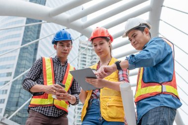 Kask güvenliği olan çok ırklı müteahhit takımı şehirdeki tablet üzerinde tartışıyorlar.