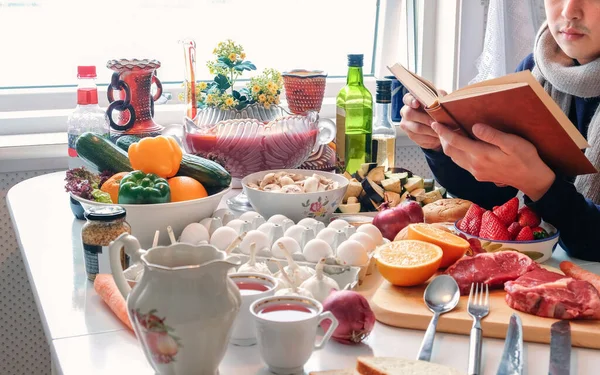 Homem Lendo Livro Sobre Mesa Jantar Com Vários Ingredientes Cozinha — Fotografia de Stock