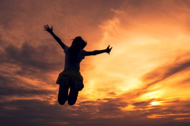 Siluet başarılı genç kadın renkli günbatımı gökyüzünde uzanmış elleri atlayarak