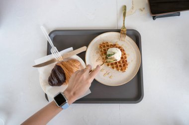 El 'in kaşık kepçeli dondurma waffle' ı ve beyaz masada kruvasan kullanışının en üst görüntüsü.