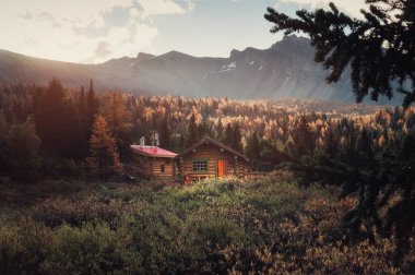 Wooden huts with rocky mountains and sunshine on autumn deep forest in the morning at Assiniboine provincial park, BC, Canada clipart
