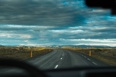 İzlanda 'da bulutlu bir günde çayırların ve lav alanlarının arasında virajlı kırsal yolda araba sürüşü görüntüsü