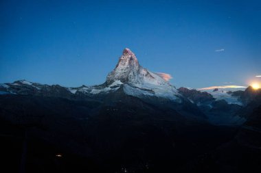 İsviçre 'deki İsviçre Alpleri arasında ay ışığında parlayan ve teleferik kullanan Matterhorn Dağı manzaralı.