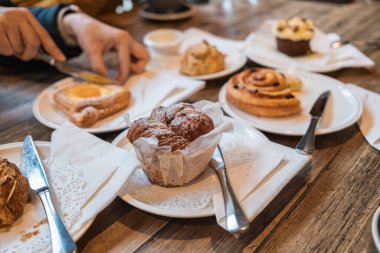 Çeşitli hamur işleri çörekleri, tarçınlı börekler, çörekler ve Danimarka çörekleri ahşap masada servis ediliyor.