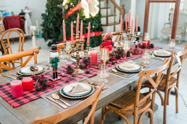 Kırmızı mumlar, mevsimlik süsler ve Noel yemeği için klasik sofra takımı ile şık bir Noel sofrası.