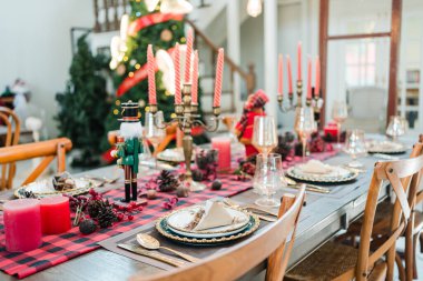 Kırmızı mumlar, mevsimlik süsler ve Noel yemeği için klasik sofra takımı ile şık bir Noel sofrası.