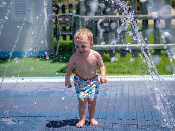 Niño corriendo bajo los aspersores de agua —  Fotos de Stock