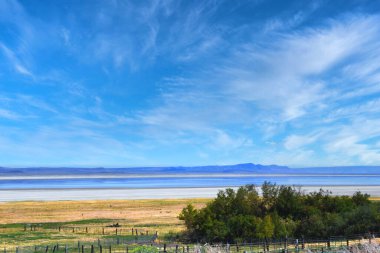 Alkali Yaz Gölü mavi gökyüzünü ve üzerindeki bulutları yansıtır. Uzakta dağların maviliği var. Merkez Oregon 'da..