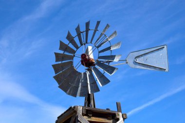Eski ahşap kule kırsal metal yel değirmenini destekliyor. Mavi gökyüzü çerçeveler.