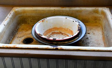 Yıkama leğenleri kirli, paslı ve lekeli bir lavaboya istiflenmiş. Pislik ve pislik bu lavaboyu temizlemeyi imkansız hale getiriyor..