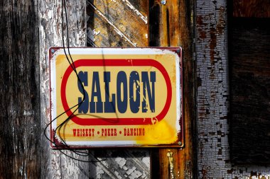 Teneke Salon tabelası eski, kapalı binanın dış duvarına çivilenmiş. Tabelanın altındaki harf sarı boya ile gizlenmiş..