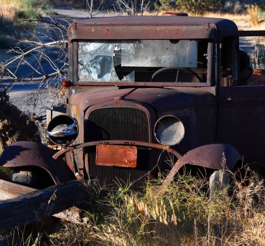 Bozulmuş ve terk edilmiş T modeli yabani otlarla kaplanmış. Pas içinde ve ön cam kırık..
