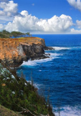 Alenuihaha kanalı Hawaii 'nin büyük adası boyunca masmavi. Dalgalar yüksek kayalıklara çarpar. Bulutlar ufukta oturuyor.