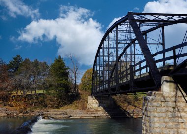 Tarihi Savaş Kartalı Mills Köprüsü, Arkansas 'ın kuzeyindeki War Eagle Nehri boyunca uzanır. Mavi gökyüzü ve bulutlar tepemizde duruyor ve küçük şelale yavaşça nehirde akıyor..