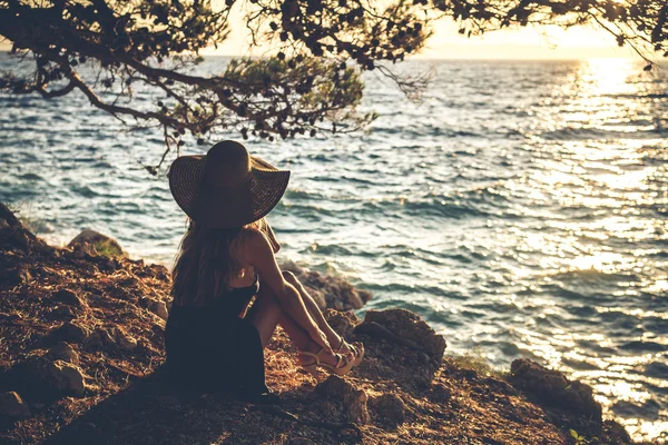 Girl in a hat sitting by the sea — Stock Photo, Image