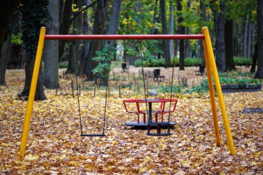 Sonbahar parkında bir sonbahar yaprakları zinciriyle zincire vurulmuş boş bir çocuk salıncağı. Arka plan bulanık. Parktaki oyun parkı.