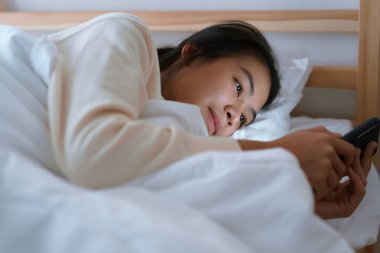 Asyalı kadın gece yatak odasında yatarken akıllı telefon kullanıyor.