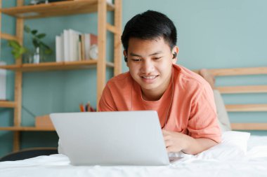 Asyalı öğrenci internette bilgisayar bilgisayarı ve kulaklıkla sabahları yatakta yatmayı öğreniyor. Evde online öğrenme kavramını kabul et