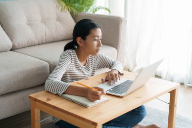 Asyalı kız internet üzerinden dizüstü bilgisayardan öğreniyor, Asyalı çocuk evde otururken ders çalışıyor. Evde çevrimiçi öğrenim kavramı 