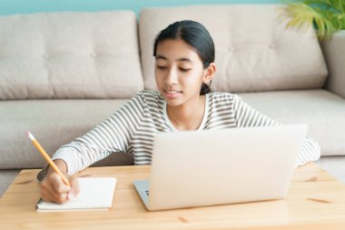 Asyalı kız internet üzerinden dizüstü bilgisayardan öğreniyor, Asyalı çocuk evde otururken ders çalışıyor. Evde çevrimiçi öğrenim kavramı 
