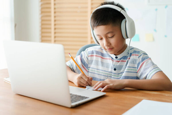 Asian little boy video call online via the internet tutor on a computer laptop with headphone. Asia man doing homework. Concept online learning at home 