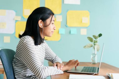 Evde oturup uzaktan öğrenme kavramını öğrenirken internetteki Asyalı kız videosu çevrimiçi internet hocası ve kulaklıkla evde otururken kulaklıkla mutlu bir Asyalı kız görüntüsü.