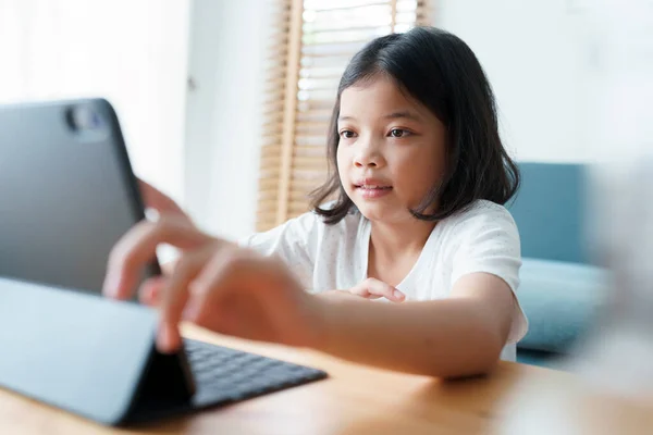 Asian little girl learning online via the internet tutor on a tablet while sitting in the living room at morning, Concept of online learning at home